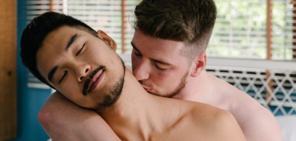 Two men, who are illustrated to be bisexual, gay or queer, are topless as one man kisses the other man's neck before engaging in sex or an intimate moment together