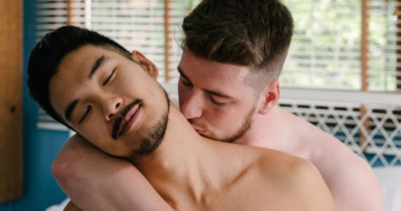 Two men, who are illustrated to be bisexual, gay or queer, are topless as one man kisses the other man's neck before engaging in sex or an intimate moment together