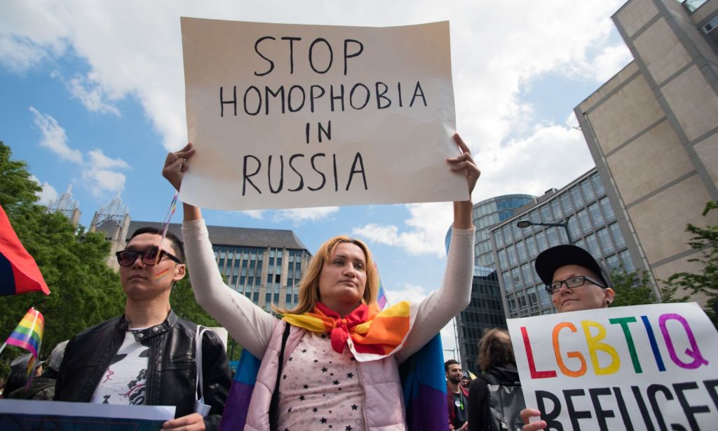 A person holds up a sign reading 'stop homophobia in Russia' while another person holds up a sign reading 'LGBTQ+ refugees' to protest against Russia's crackdown on queer people