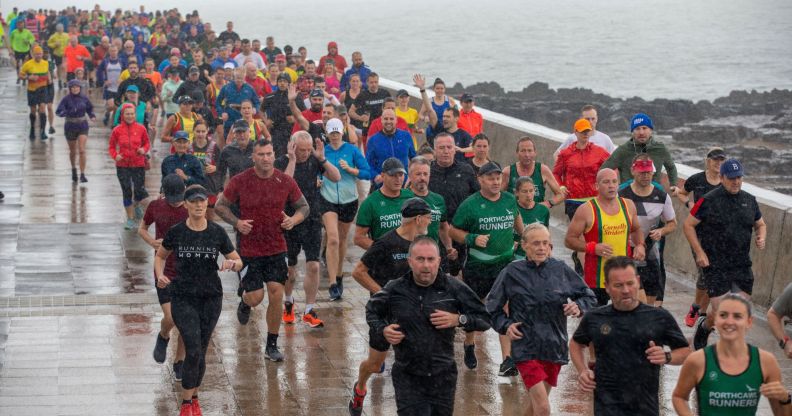 People taking part in a Parkrun in Wales. The image shows many people running on a wet, rainy day by the sea.
