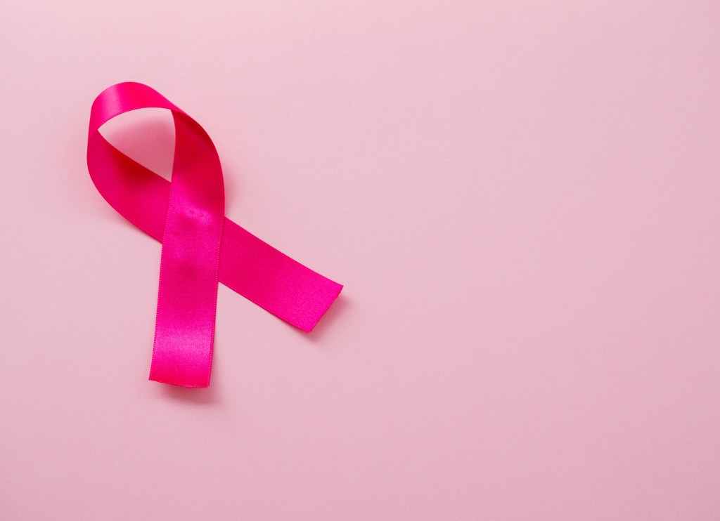 A pink ribbon for breast cancer awareness is pictured against a pink background.