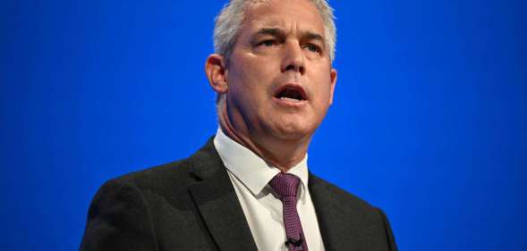 Steve Barclay giving a speech at the Conservative party conference in Manchester in October 2023. He is pictured wearing a dark suit and tie against a blue background.