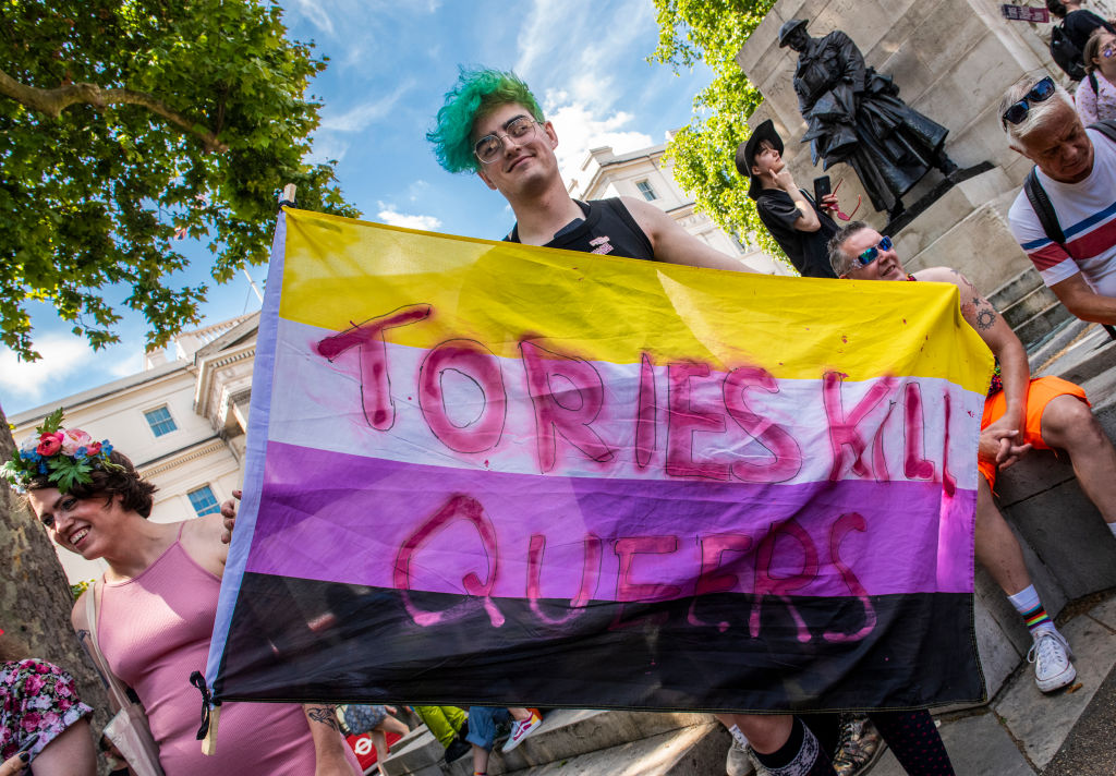 A member of the LGBTQ+ with green hair holds a banner with the words Tories Kill Queers and protests against the lack of rights and healthcare for transgender people. 