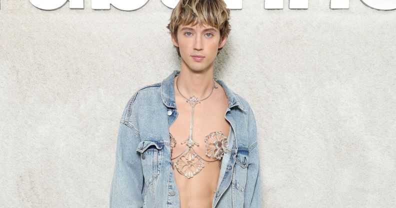 Australian singer Troye Sivan wears sparkly body jewellery on his bare chest and a light denim jacket