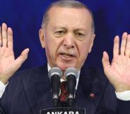 Turkey's president Recep Tayyip Erdoğan, who has a history of making anti-LGBTQ+ remarks, wears a suit and tie as he holds up both his hands while speaking into a microphone