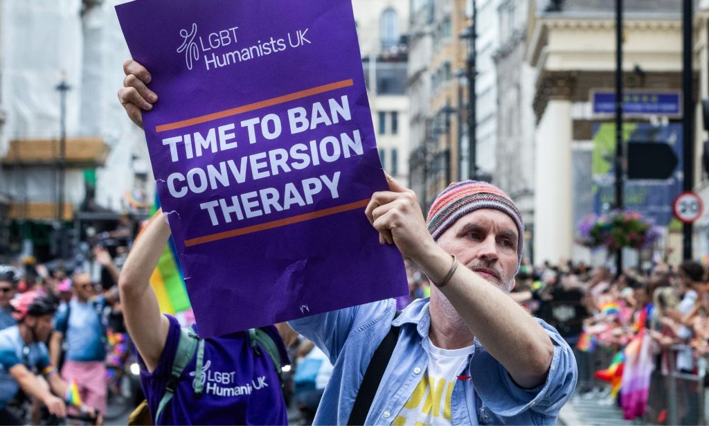 A protestor holds a sign reading "time to ban conversion therapy."