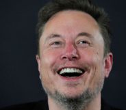 Elon Musk laughing infront of a grey background.