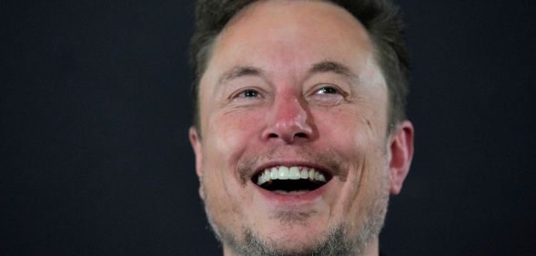 Elon Musk laughing infront of a grey background.