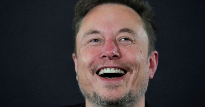 Elon Musk laughing infront of a grey background.