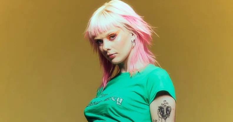 Pop singer Girli in a green top standing against a yellow background.