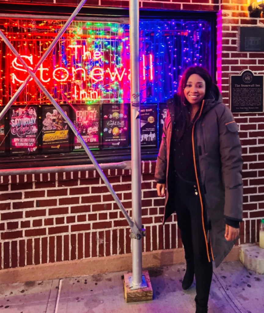 This is an image of a Black woman, Jacqui Rhule-Dagher outside the Stonewall Inn in New York City. 