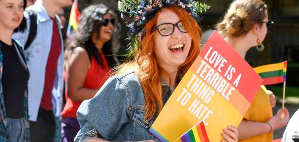 An LGBTQ+ activist holds a sign saying 'love is a terrible thing to hate'