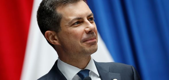 Pete Buttigieg smiling while on the stand of a press conference stage.