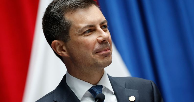 Pete Buttigieg smiling while on the stand of a press conference stage.