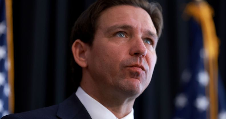 Ron DeSantis looking upwards while American flags stand beside him.