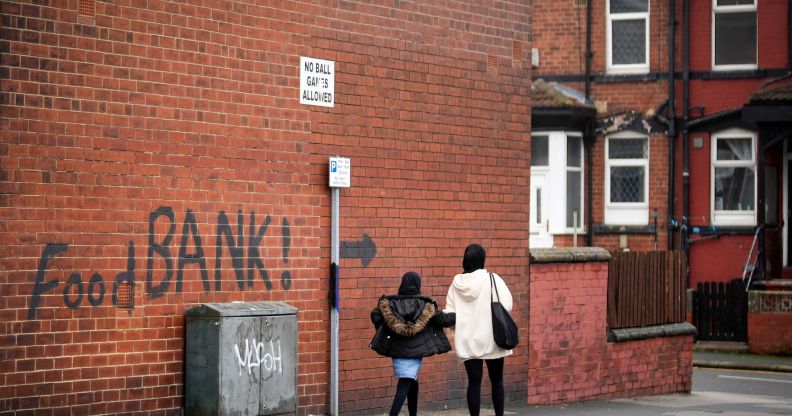 A mother and child can be seen walking past a food bank sign.