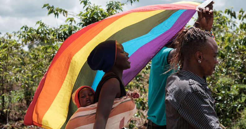 LGBTQ+ refugees from Uganda and other African countries walk together outside while they are living in Kenya and waving a rainbow flag