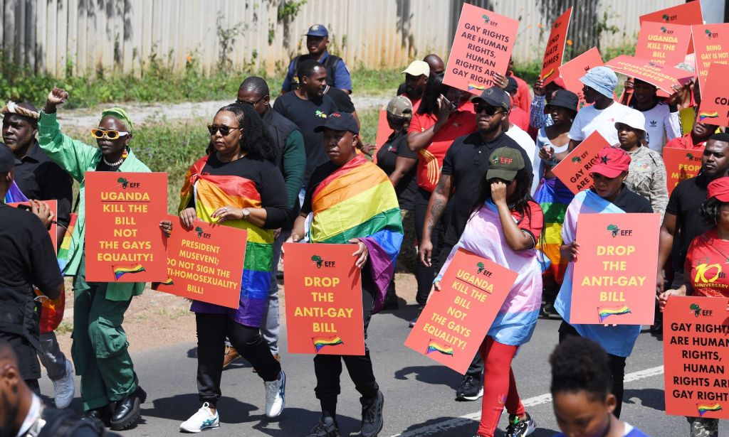 Several people hold up signs denouncing anti-LGBTQ+ legislation and persecution in Uganda during a protest