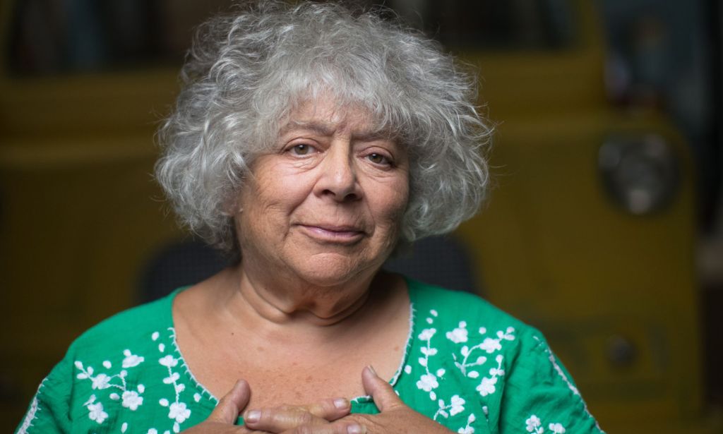 Actor Miriam Margoyles wears a green shirt with while spots on it while her hands cover her chest over her heart