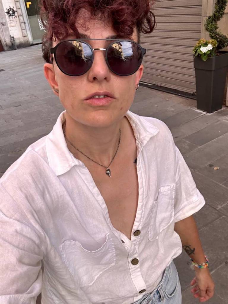 Marley, a non-binary person who came out and transitioned during a long-term relationship, posts with their white shirt slightly open and with sunglasses on their face