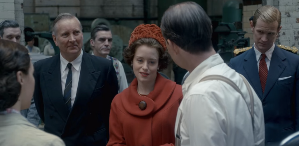 Claire Foy as Queen Elizabeth II in The Crown, wearing a red hat, red coat and with a short, curly brown hairstyle.