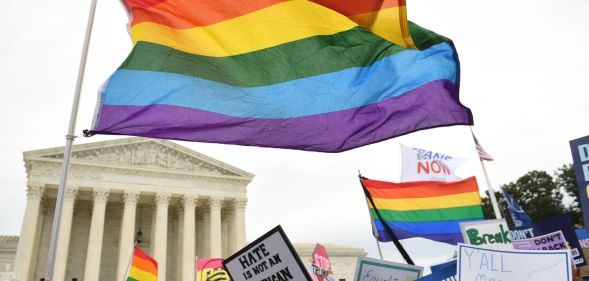 An LGBTQ+ flag waving above a state capitol building.