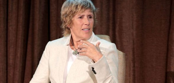 Lesbian swimmer Diana Nyad wears a cream suit while speaking on stage