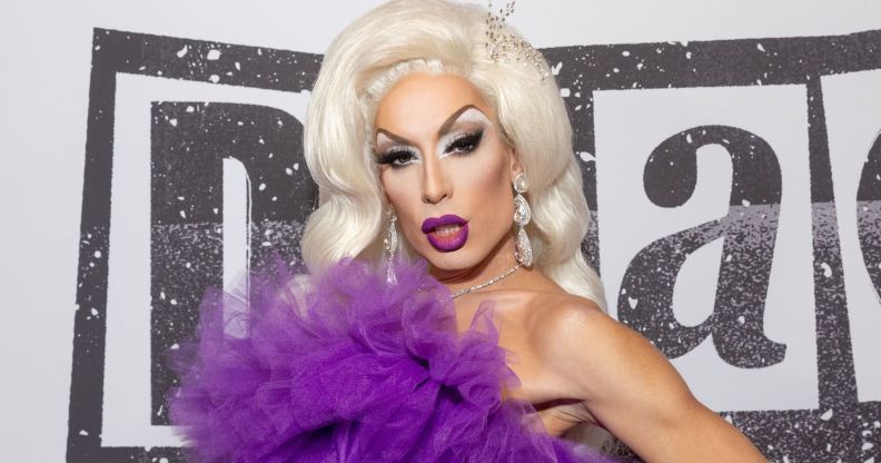 Drag Race star Alaska wears a purple dress and blonde wig.