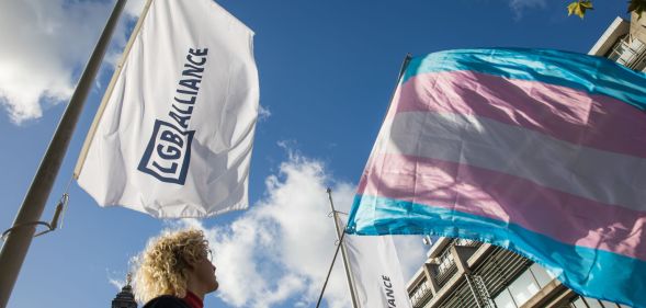 Image of protester waving a trans flag alongside the LGB Alliance flag