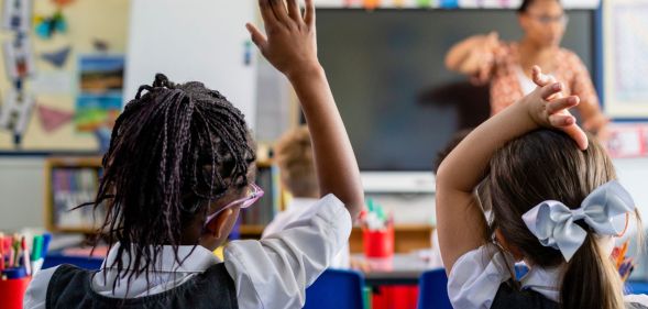 Two children raise their hands in a school classroom.