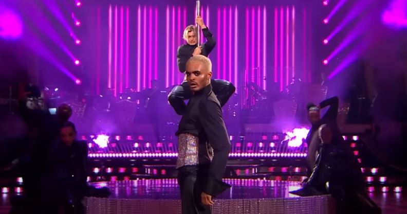 Layton Williams and Nikita Kuzmin wear matching sparkly corsets and black outfits as Williams stands in front of Kuzmin, who is clutching a pole, during a performance on BBC's Strictly Come Dancing