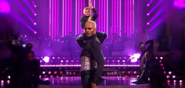 Layton Williams and Nikita Kuzmin wear matching sparkly corsets and black outfits as Williams stands in front of Kuzmin, who is clutching a pole, during a performance on BBC's Strictly Come Dancing