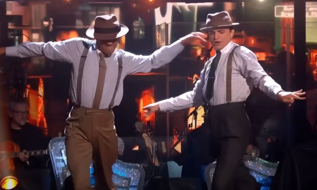 Layton Williams and Nikita Kuzmin wear outfits composed of a shirt, suspenders, trousers and hat as they dance together during a performance on BBC's Strictly Come Dancing