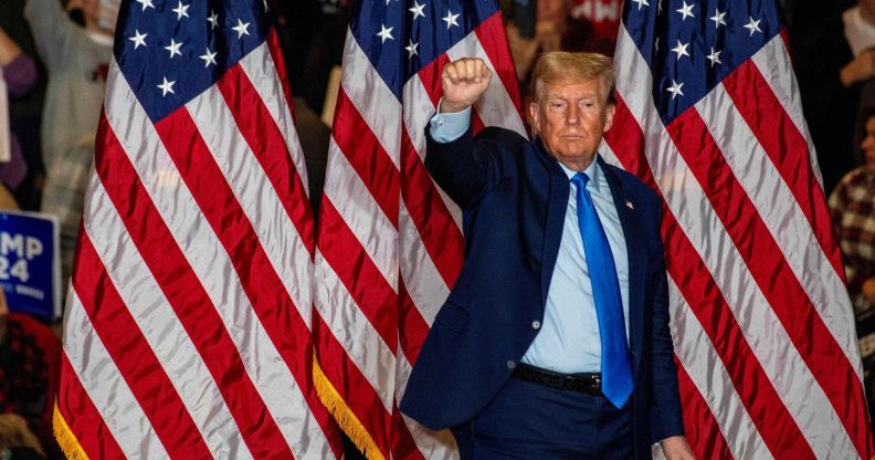 This picture shows Donald Trump standing against three American flags holding a raised fist to supporters.