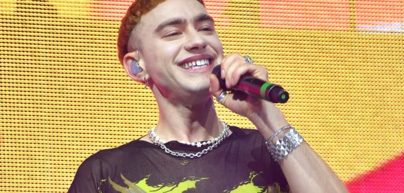 Olly Alexander wears a yellow and black shirt as he sings into a microphone while on stage