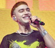 Olly Alexander wears a yellow and black shirt as he sings into a microphone while on stage