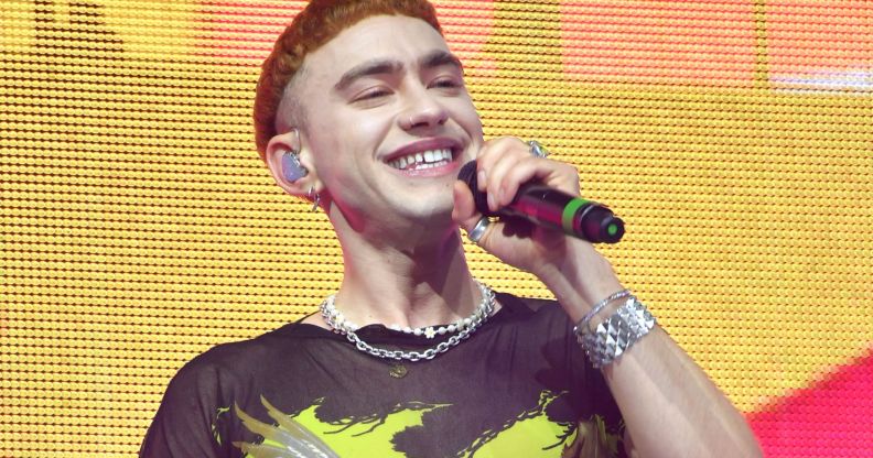 Olly Alexander wears a yellow and black shirt as he sings into a microphone while on stage