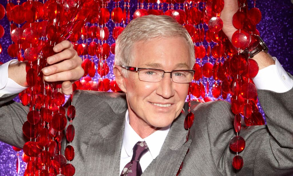 Paul O'Grady  wears a grey suit as he poses with reflective surfaces. He is among the LGBTQ+ stars and allies that died in 2023
