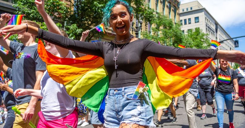 A person wears a rainbow coloured cape as they walk in an LGBTQ+ pride celebration in the US state of Oregon
