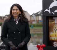 Former home secretary Suella Braverman, wearing a black coat, smiles awkwardly, as she's presented with The Last Leg's "D**k of the Year" award which is displayed on a sign behind her