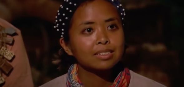 A screenshot from Survivor 41 of contestant Erika Casupanan wearing a light coloured shirt and dark headband with pearls on it