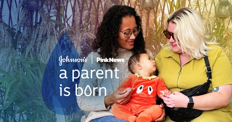 This is an image with 2 women holding a baby. The woman on the left is wearing a grey jumper. She has long dark hair and is wearing glasses. The woman on the right has bright blonde hair and is wearing sunglasses. The baby in the middle is wearing an orange onesie. Over the image in white text reads "JOHNSON'S, PINKNEWS A PARENT IS BORN"
