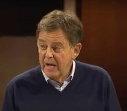 Christian pastor dropped by radio network, Alistair Begg, addresses the crowd from a stage in his sermon on Sunday (28 January) he is an older man wearing a dark blue sweater over a buttoned up shirt.