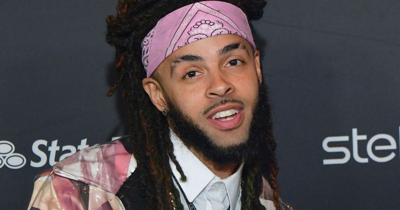 A man with dreadlocks and a chin strap beard wearing a pink bandana poses during a red carpet event.
