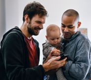 Two men holding a baby watch a video on their mobile phone.