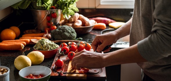 Human hands slicing tomatoes over a wooden table for a vegan meal