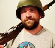 A man wearing a green army helmet holds a wooden rifle over his shoulder.