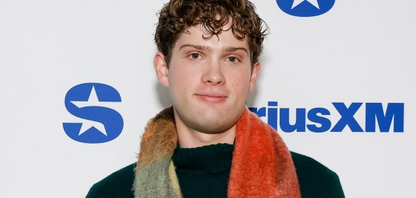 Leo Reich, a curly haired man with a slightly fluffy red, yellow and blue scarf, he's wearing a black jumper.