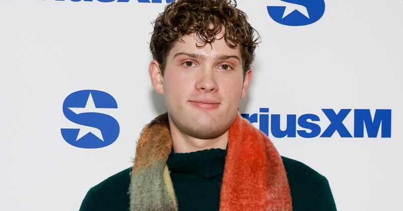 Leo Reich, a curly haired man with a slightly fluffy red, yellow and blue scarf, he's wearing a black jumper.
