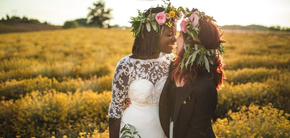 Stock image of a lesbian wedding, with one woman wearing a dress and carrying flowers, and another wearing a black suit jacket